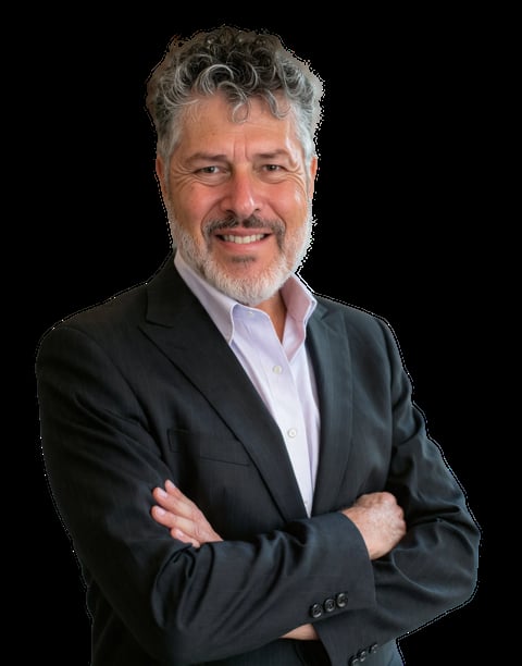 Professional headshot of a middle-aged man with gray hair and beard wearing a black blazer and light blue shirt, standing with crossed arms against a black background