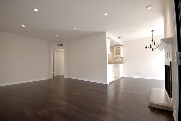 Empty modern living room with dark hardwood floors, white walls, recessed lighting, and a fireplace