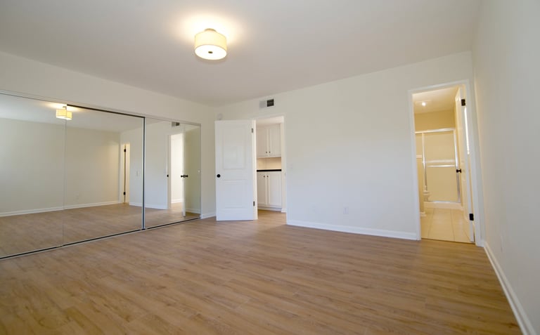 Empty apartment interior with hardwood floors, white walls, ceiling light, and multiple doorways leading to other rooms