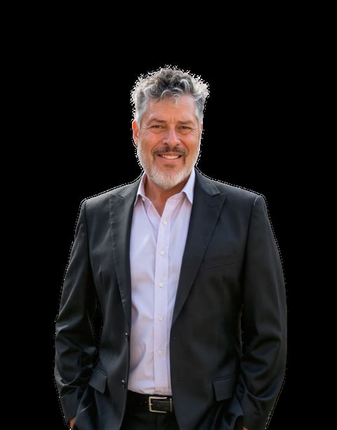 Middle-aged man with gray hair and beard wearing a dark blazer over a light pink button-up shirt, smiling at camera against black background