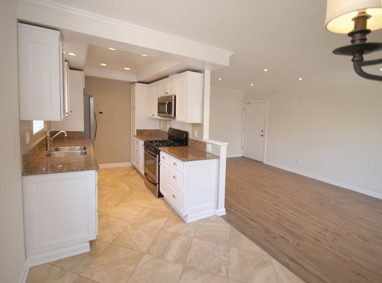 Modern kitchen with white cabinetry, granite countertops, and stainless steel appliances adjoining an open dining area with hardwood flooring