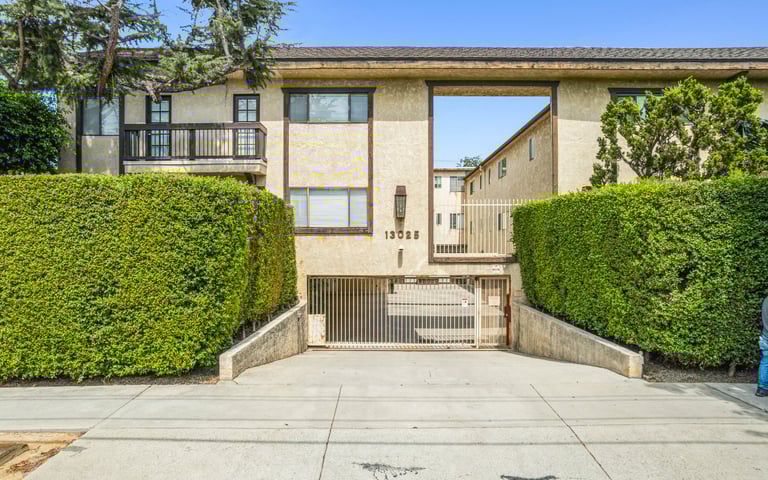 Modern townhouse with stone facade, metal gated entrance, and tall green hedges flanking a concrete driveway