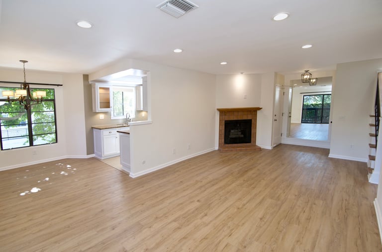 Spacious open-concept living room with wood flooring, fireplace, kitchen area, recessed lighting, and large windows